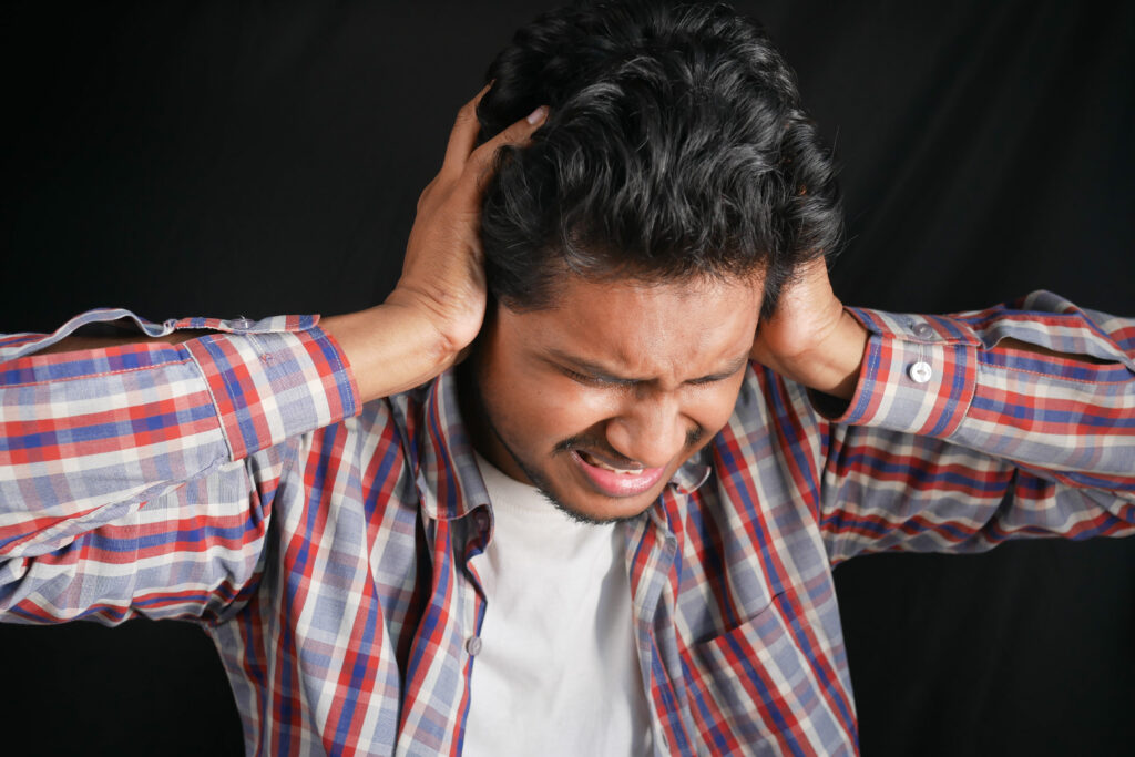 young man having ear pain touching his painful ear isolated on black